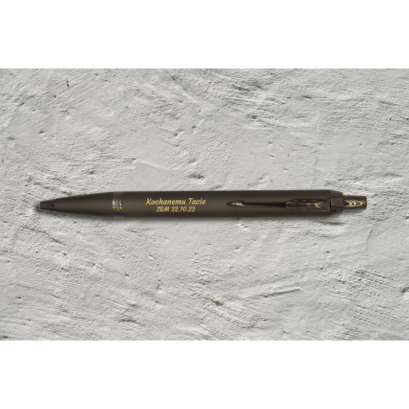 Brązowy długopis Parker IM Professionals Monochrome Bronze z grawerem „Kochanemu Tacie – Z&M 22.10.22” na tle surowego betonu.