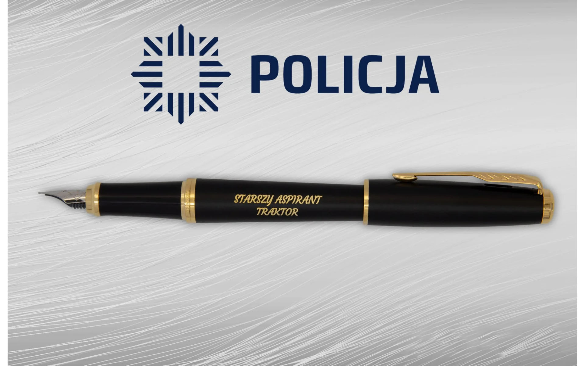 Pióro wieczne Parker Urban Muted Black GT [1931601] – eleganckie czarne pióro z pozłacanymi wykończeniami, ozdobione grawerem „STARSZY ASPIRANT TRAKTOR”, zaprezentowane na tle z logo Policji.