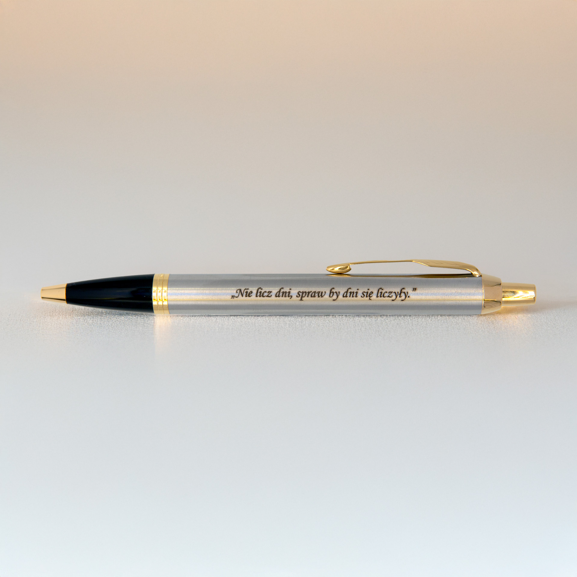 Długopis Parker IM Brushed Metal GT (1931670) z grawerem „Nie licz dni, spraw by dni się liczyły.” sfotografowany na jasnym tle w ciepłym, miękkim świetle.