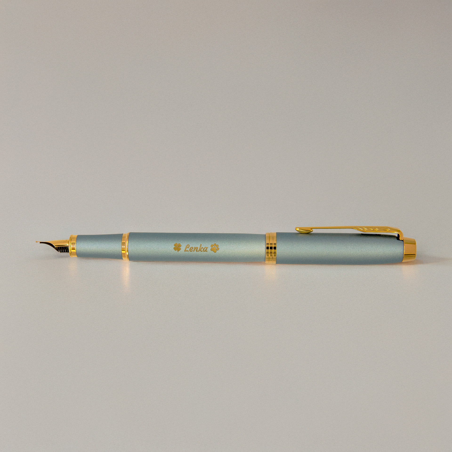 Pióro wieczne Parker IM Rituals Turquoise Green (2203892) z grawerem „Lenka” i motywem łapek, sfotografowane na jasnym tle w miękkim, ciepłym świetle.