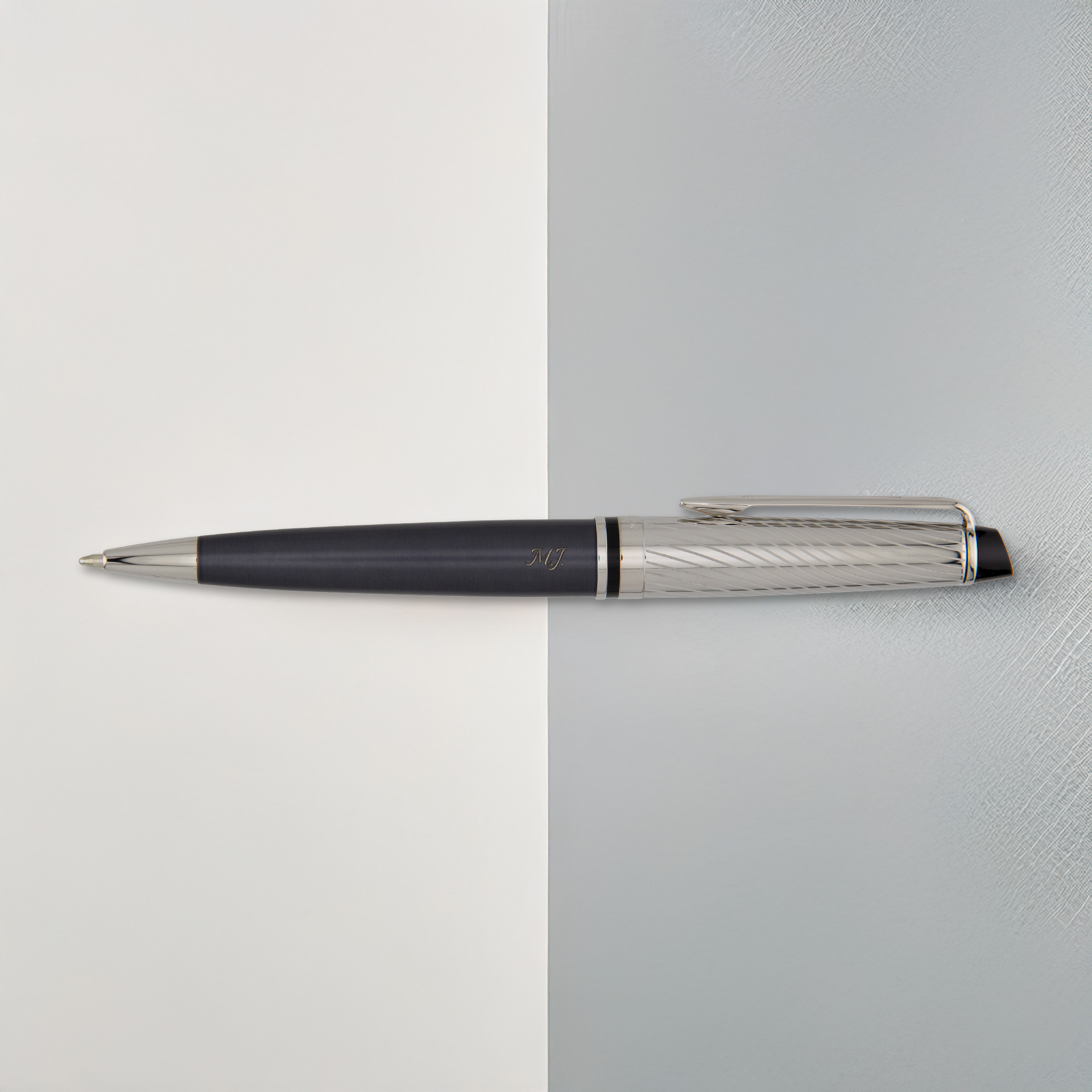 Długopis Waterman Expert Deluxe w grafitowym wykończeniu leży na dwukolorowym tle, ukazując metaliczną fakturę skuwki.